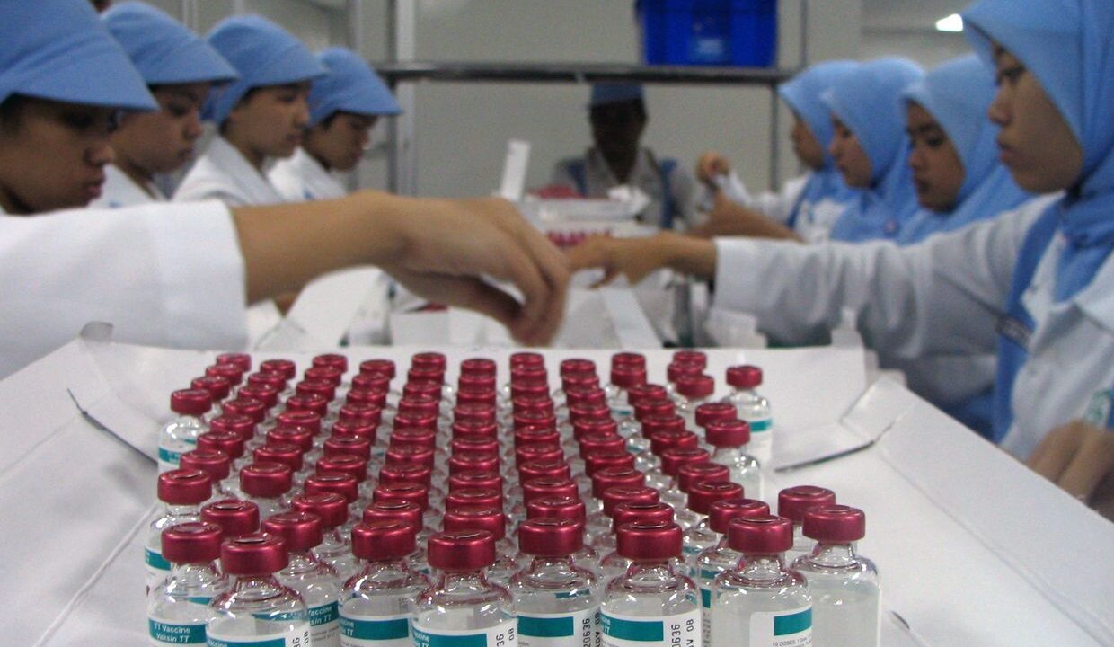Workers handling rows of vaccine vials in a laboratory